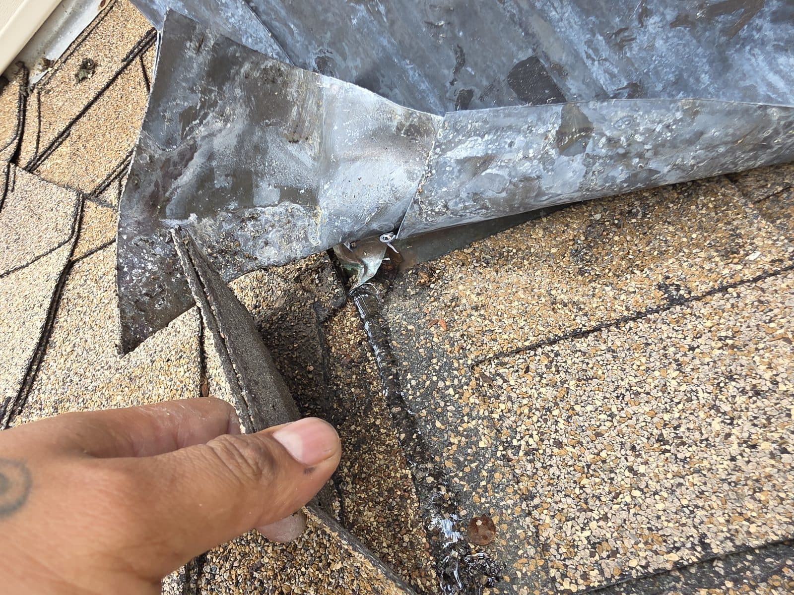 The lead flashing lifted by hand at the chimney base: the shingles run underneath it, so the metal was laid over the roof surface, not woven into it.