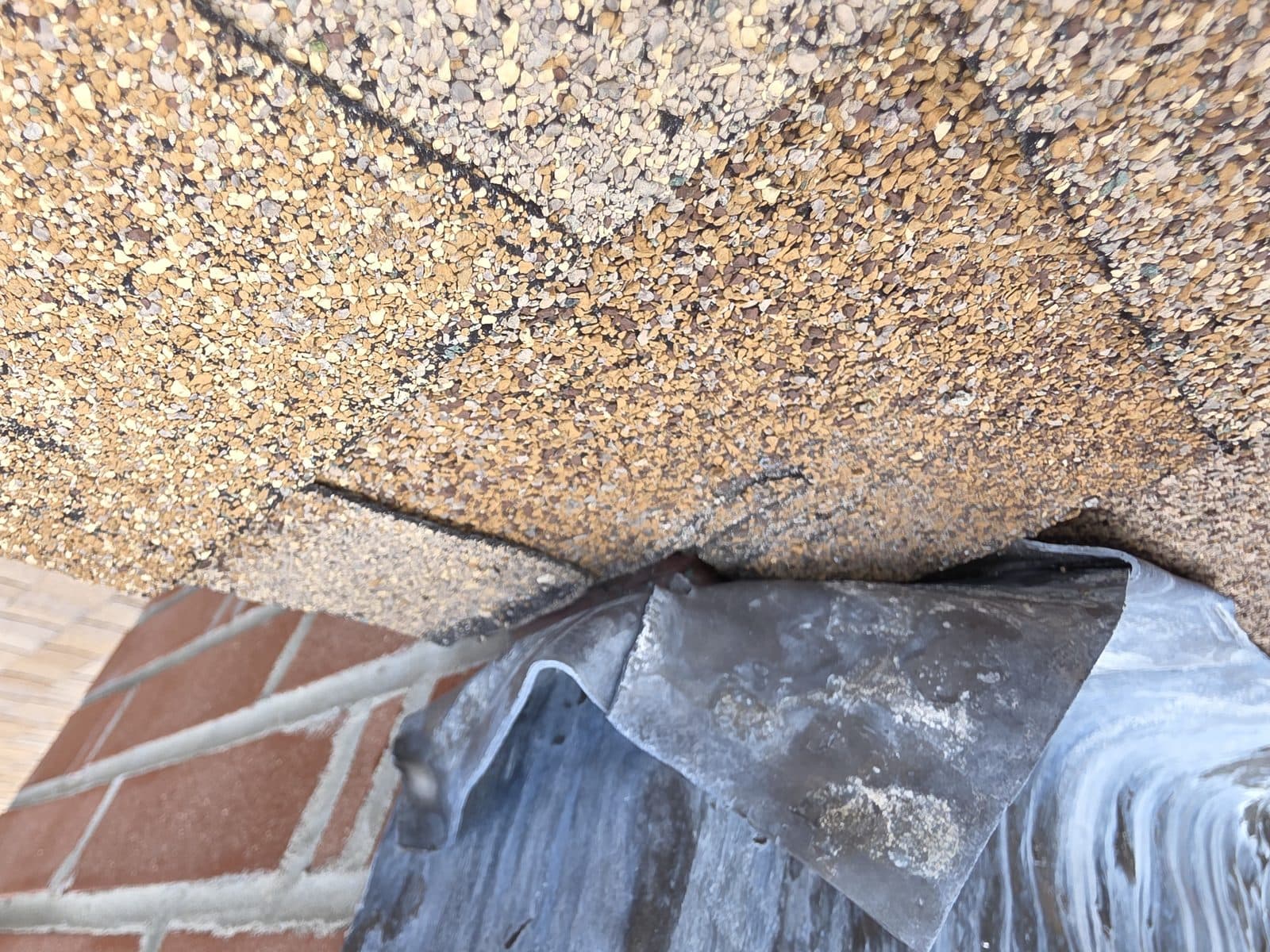Lead chimney flashing sitting on top of the shingles instead of under them, with the sealant bead along the top edge cracked open.