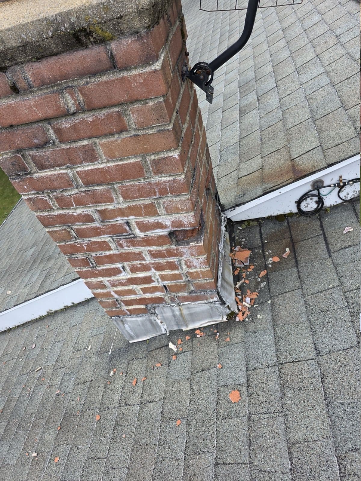 Brick chimney with metal flashing and masonry debris on the shingles