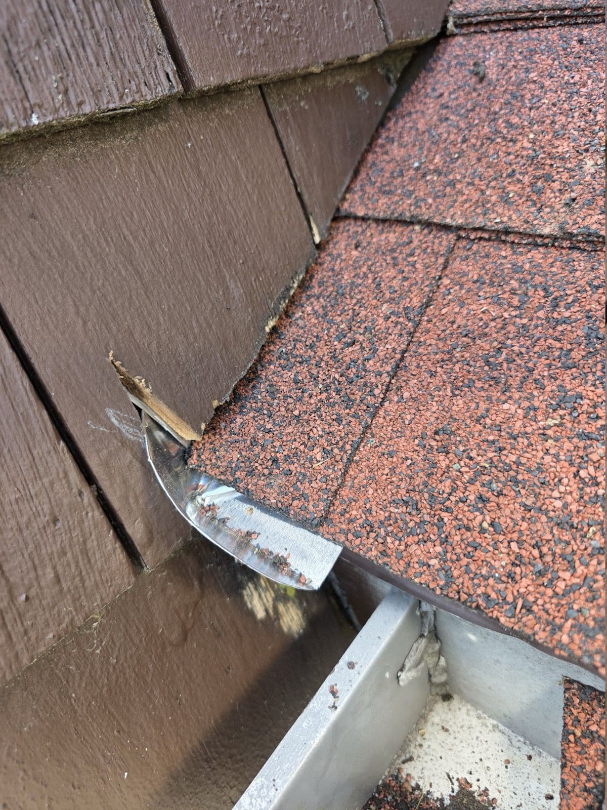 Metal flashing detail beside red shingles and wood siding in New Britain