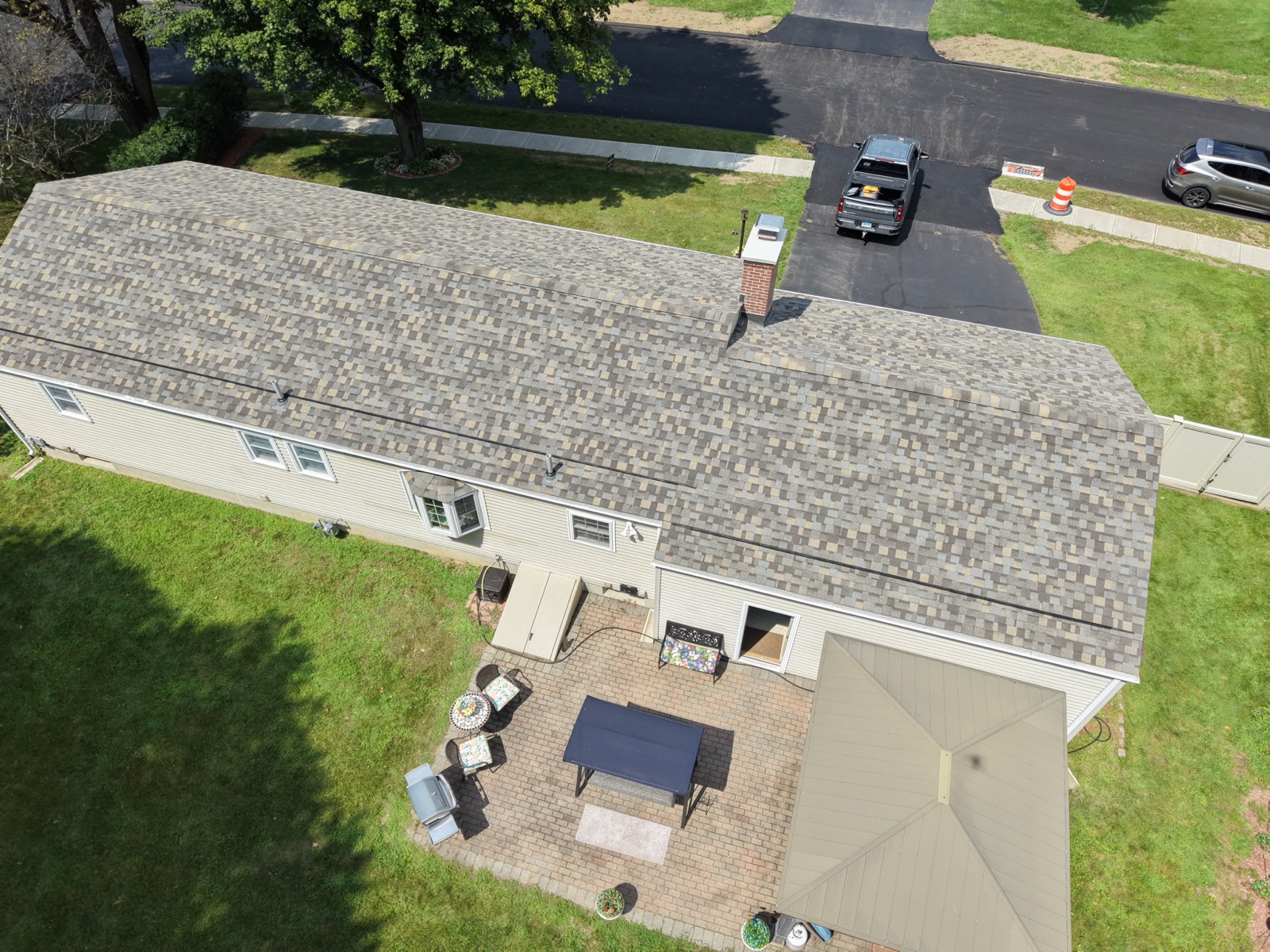 Rear aerial view of a finished shingle roof replacement in Enfield, CT with patio and yard below